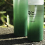 Two green bottles with 'haruharu wonder' branding on a stone surface with blurred greenery in the background.
