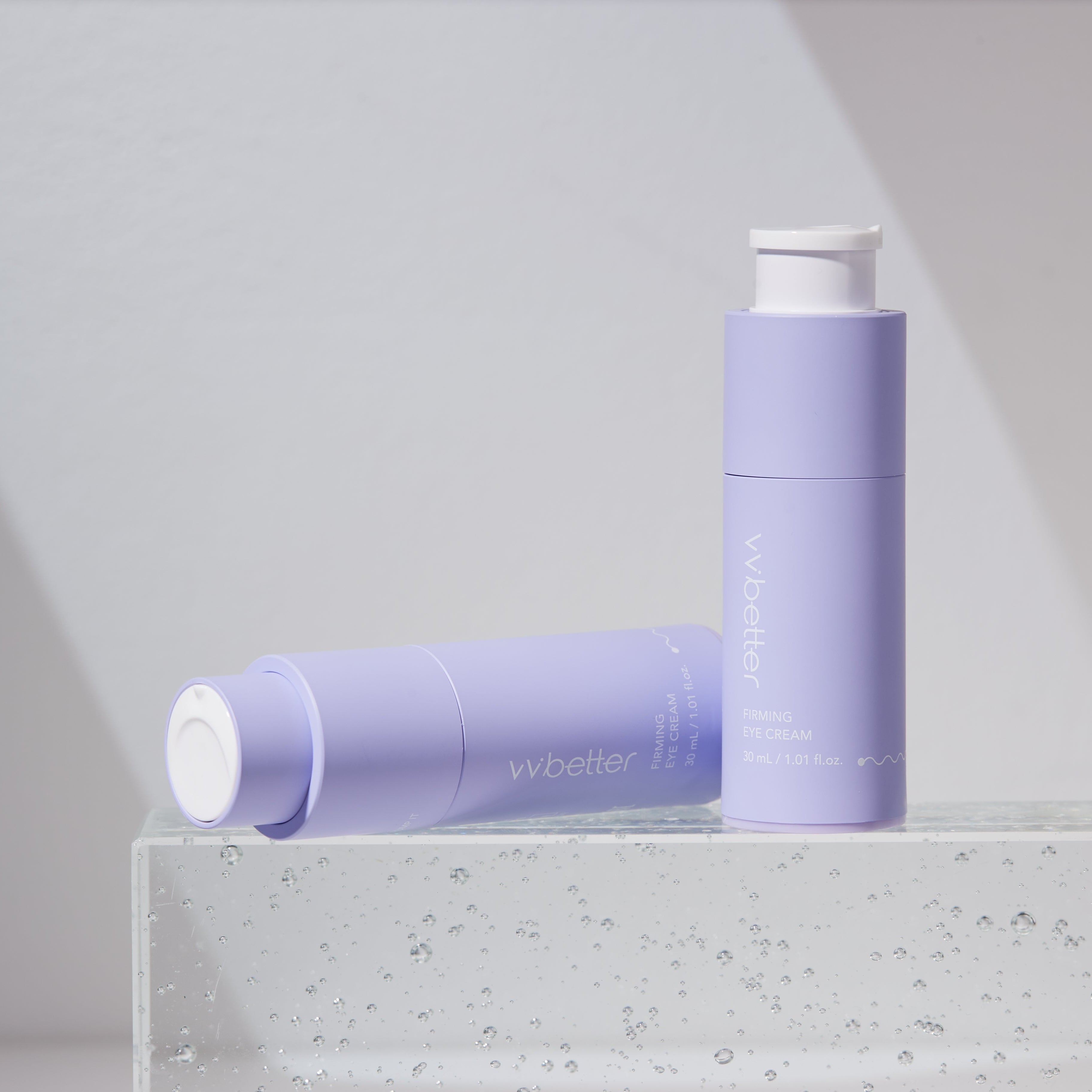 Two purple skincare bottles with white caps on a clear surface against a light gray background